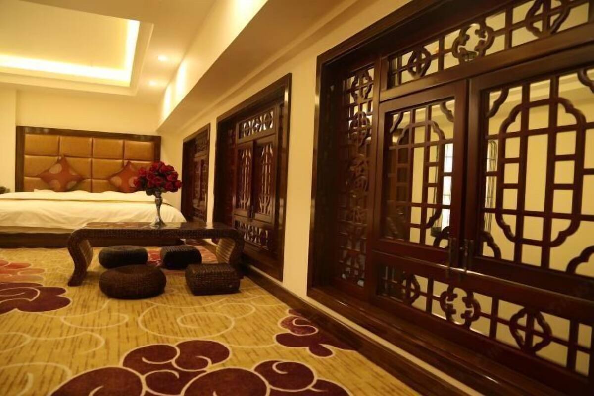 Habitación de hotel con cama, un florero con flores rojas, un biombo de madera y una alfombra estampada.
