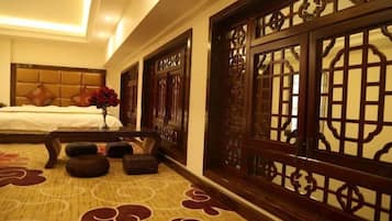 A hotel room with a bed, a vase with red flowers, a wooden screen, and a patterned carpet.