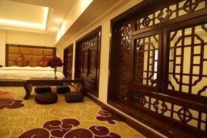 Ein Hotelzimmer mit einem Bett, einer Vase mit roten Blumen, einem Holzschirm und einem gemusterten Teppich.