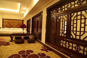Habitación de hotel con cama, un florero con flores rojas, un biombo de madera y una alfombra estampada.