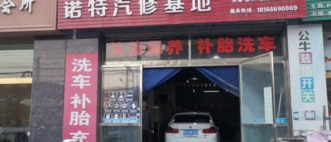 Un lavadero de coches con un letrero rojo y blanco, un coche blanco en su interior y una moto estacionada afuera.