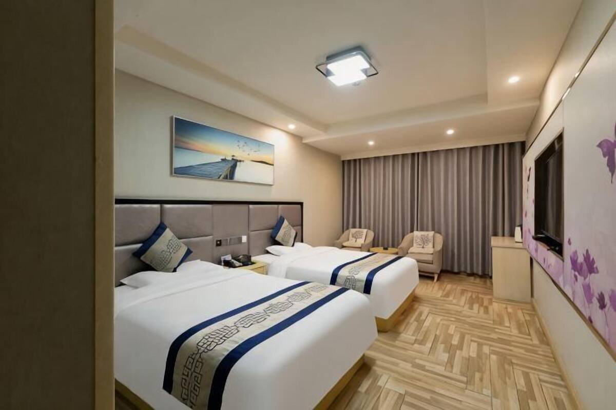 Habitación de hotel con dos camas, un escritorio, una silla, un televisor y un cuadro en la pared.
