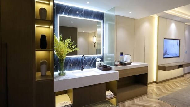 A modern bathroom with a large mirror, marble countertop, and a flat-screen TV mounted on the wall. - Shiji Jiamei Hotel (Suide)