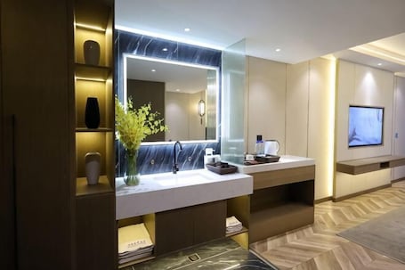 A modern bathroom with a large mirror, marble countertop, and a flat-screen TV mounted on the wall.. Shiji Jiamei Hotel