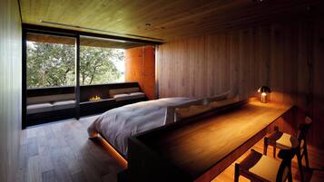 A modern bedroom with a large bed, a wooden bench, and a view of trees through a sliding door.