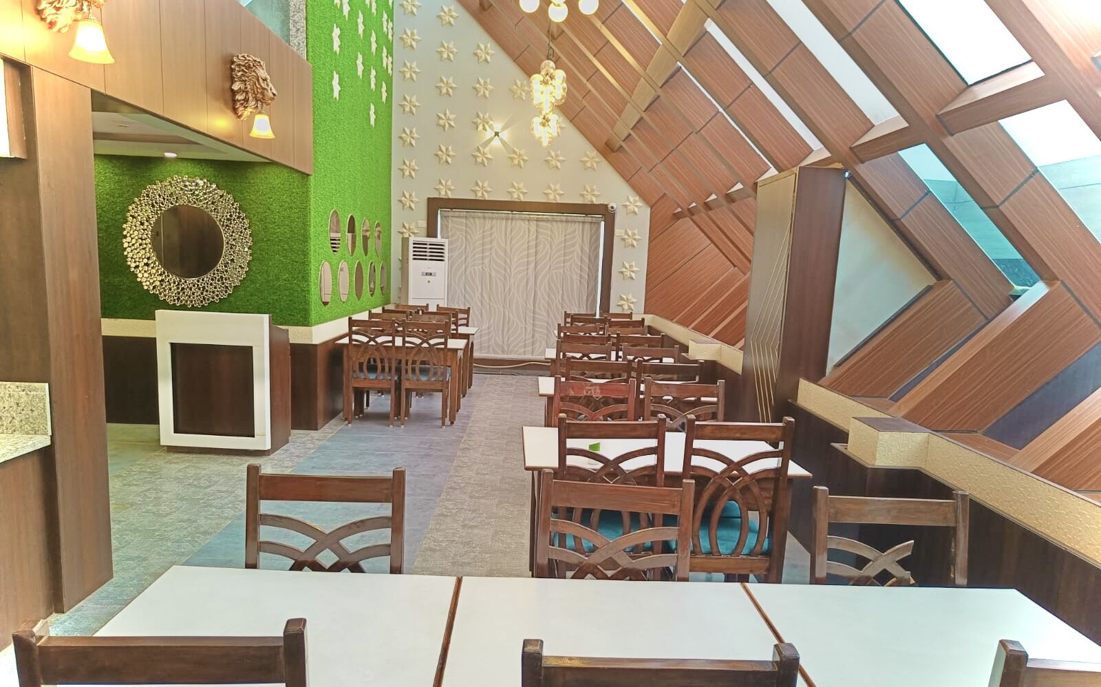 A dining area with wooden tables and chairs, a green wall with a decorative mirror, and a sloped ceiling with skylights.