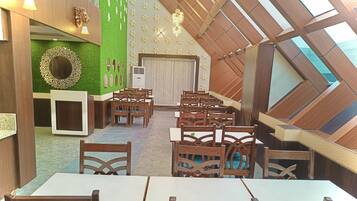 A dining area with wooden tables and chairs, a green wall with a decorative mirror, and a sloped ceiling with skylights.