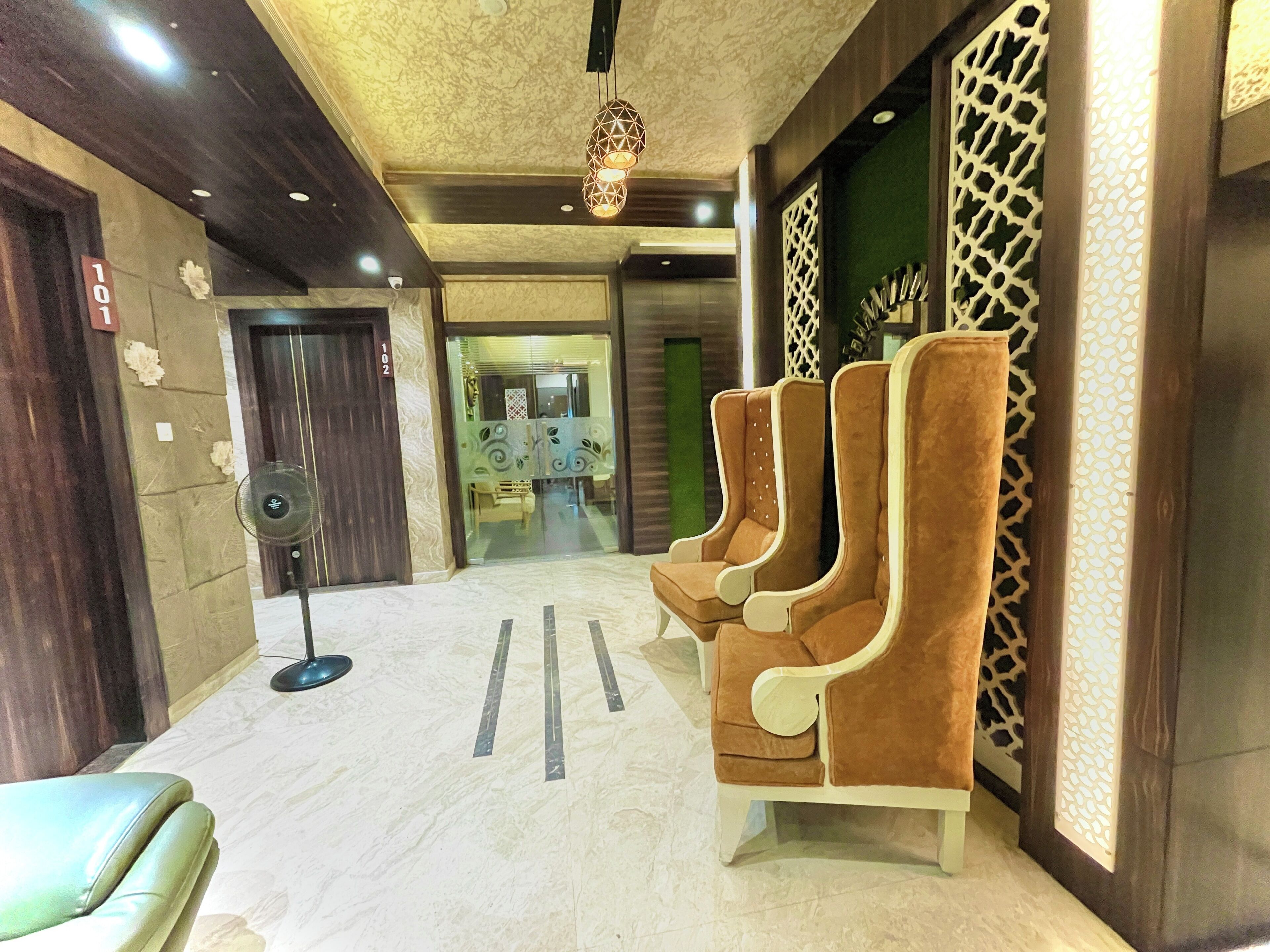 Een hotel lobby met een receptiebalie, een zithoek met bruine stoelen, en een decoratieve muur met een geometrisch patroon.