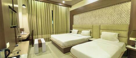 A hotel room with two beds, a desk with a coffee maker, a TV, and a ceiling fan.
