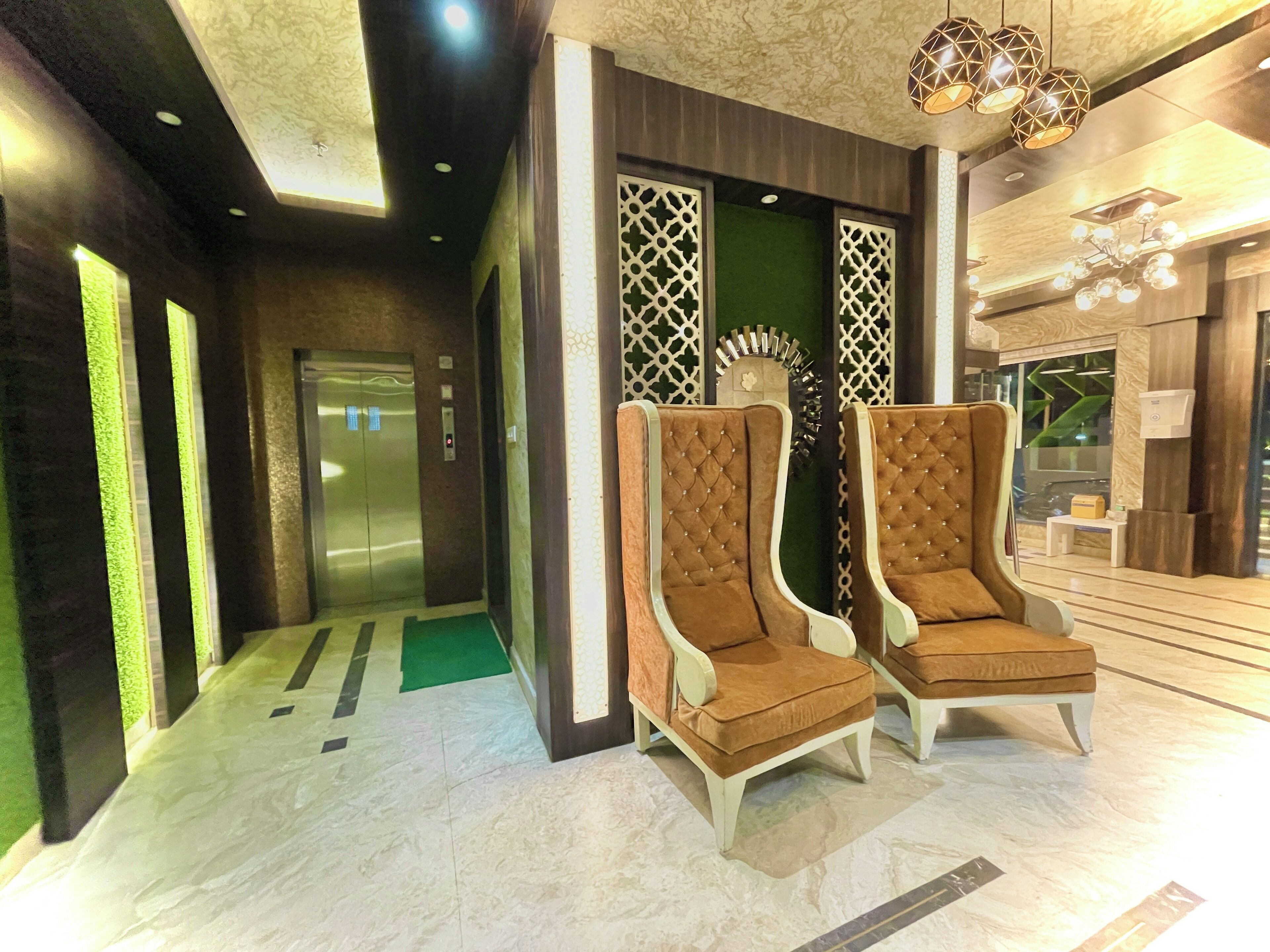 A modern lobby with a reception desk, two upholstered armchairs, a decorative wall panel, and an elevator.
