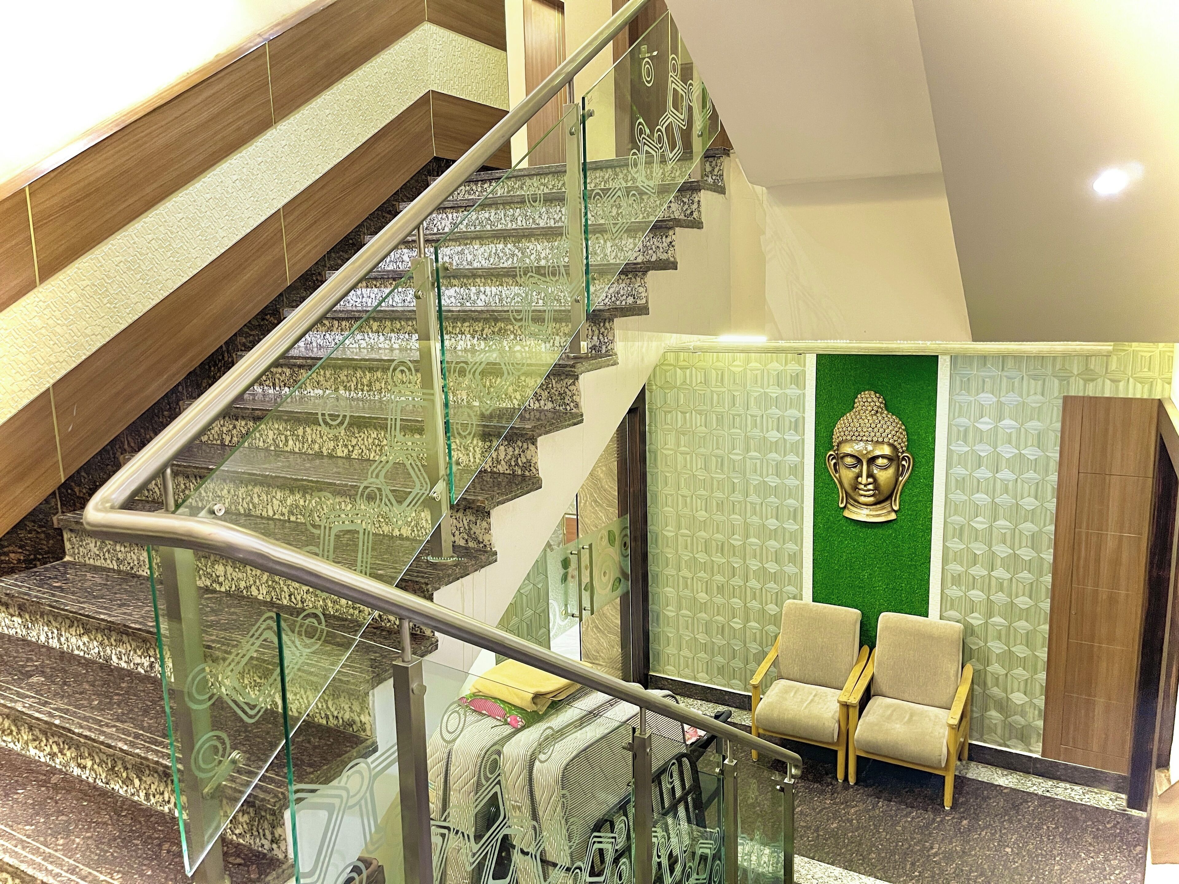 A modern hotel lobby with a glass staircase, a Buddha statue, and two beige chairs.