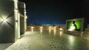 Una terraza en la azotea con baldosas estampadas, una zona de estar con una estatua y vistas de la ciudad iluminada de noche.