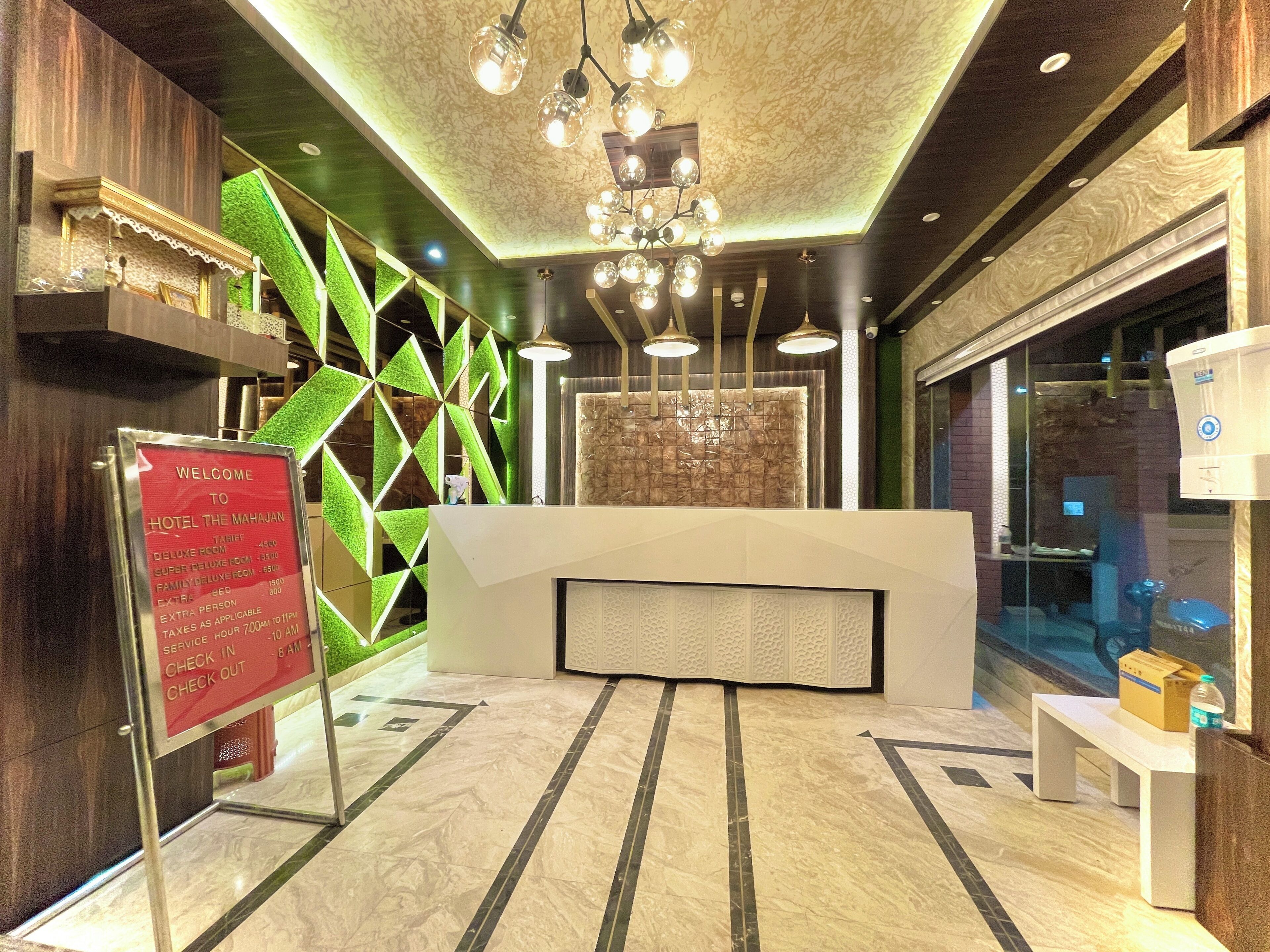 Uma área de recepção de hotel com design moderno, incluindo um balcão de recepção, uma parede geométrica verde e um candelabro.