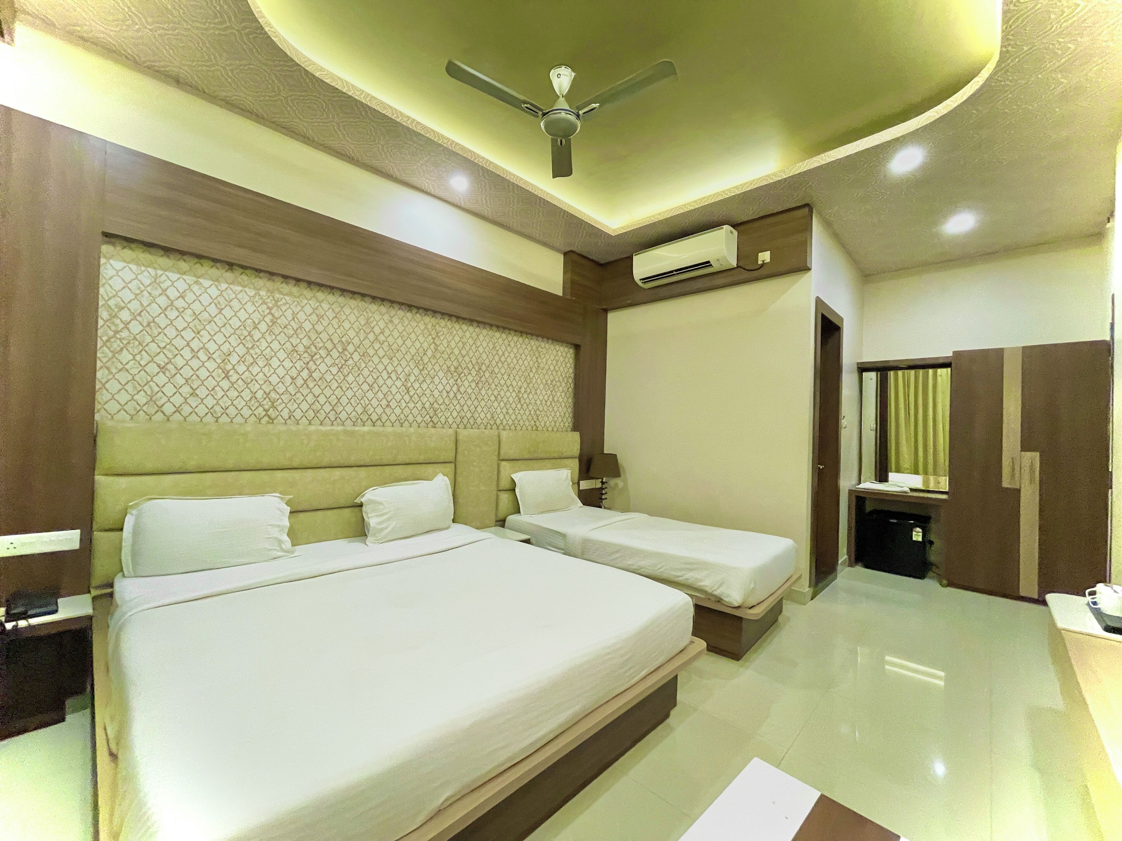 Habitación de hotel con una cama grande, dos camas más pequeñas, un ventilador de techo, un aire acondicionado, un espejo y un armario.