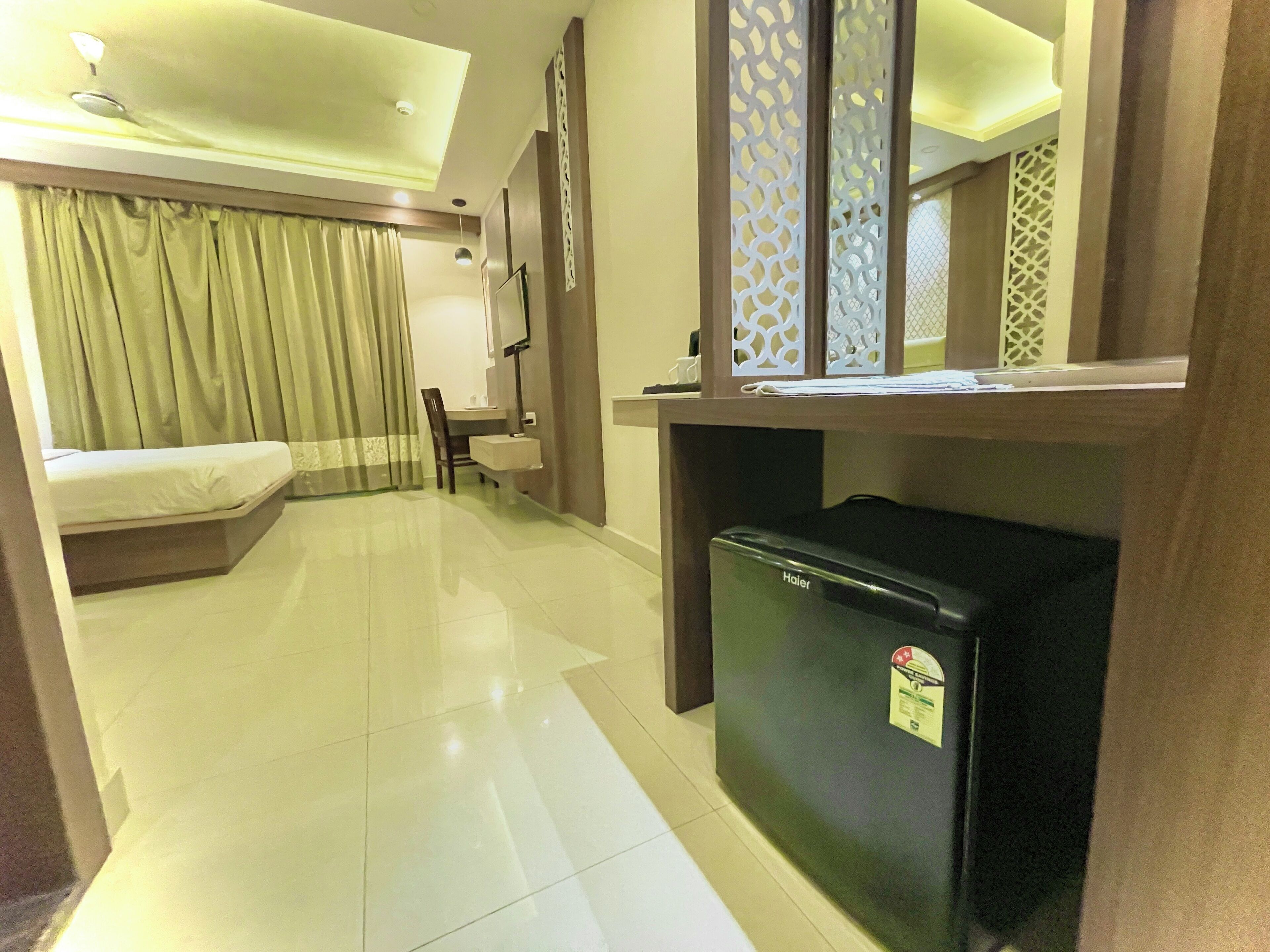 Habitación de hotel con cama, escritorio, silla, refrigerador y un separador decorativo.