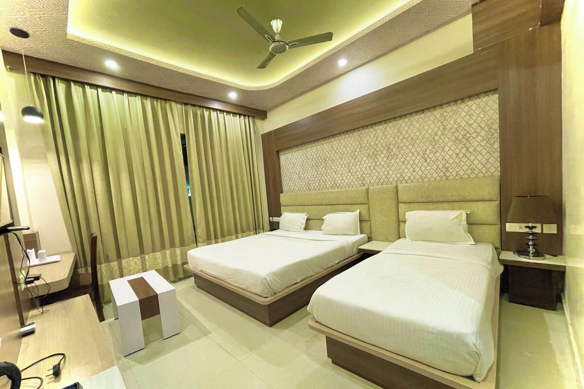 Habitación de hotel con dos camas, un ventilador de techo, una mesita de noche con lámpara y un ventanal con cortinas.