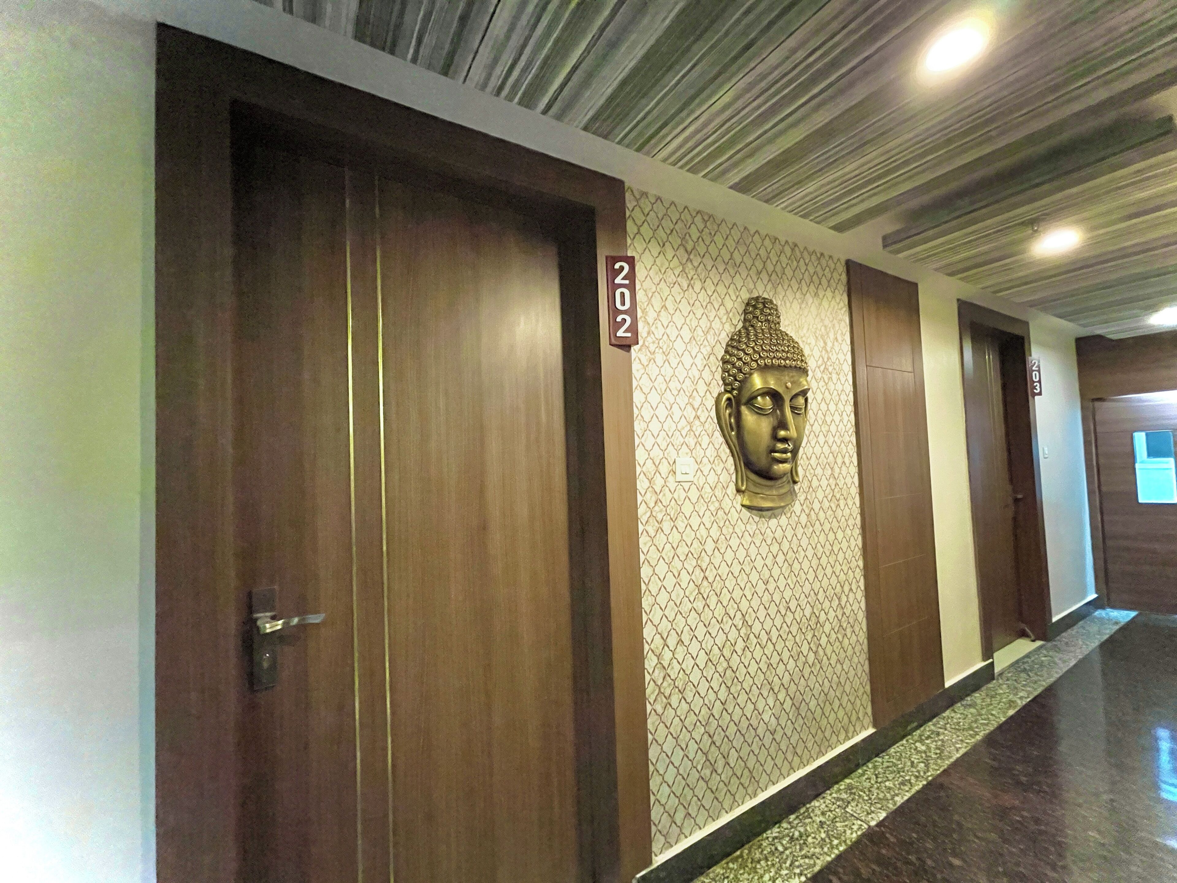 A hallway with wooden doors, a Buddha head sculpture, and a number sign.