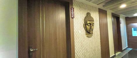 A hallway with wooden doors, a Buddha head sculpture, and a number sign.