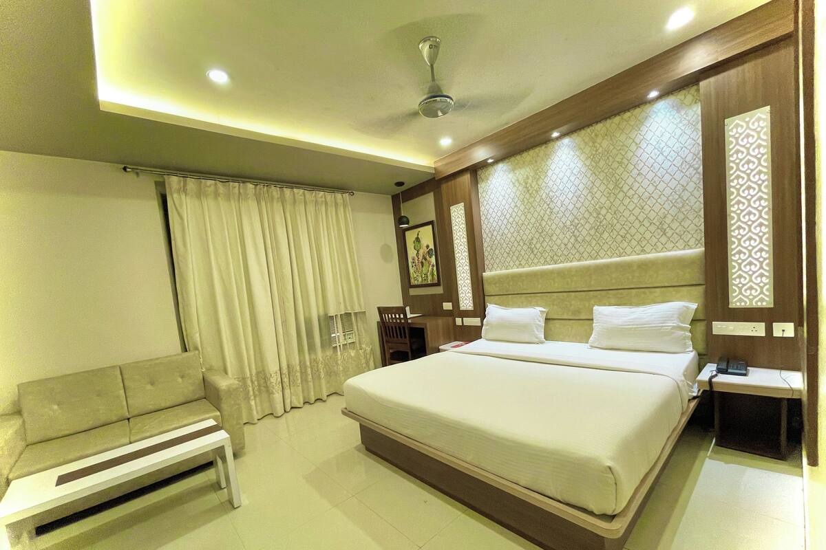 Una habitación de hotel con una cama grande, una mesita de noche, una silla y un ventilador de techo.
