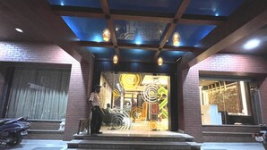 Fachada de vidrio en la entrada de un edificio, con escalones que conducen a la puerta y un guardia de seguridad afuera.