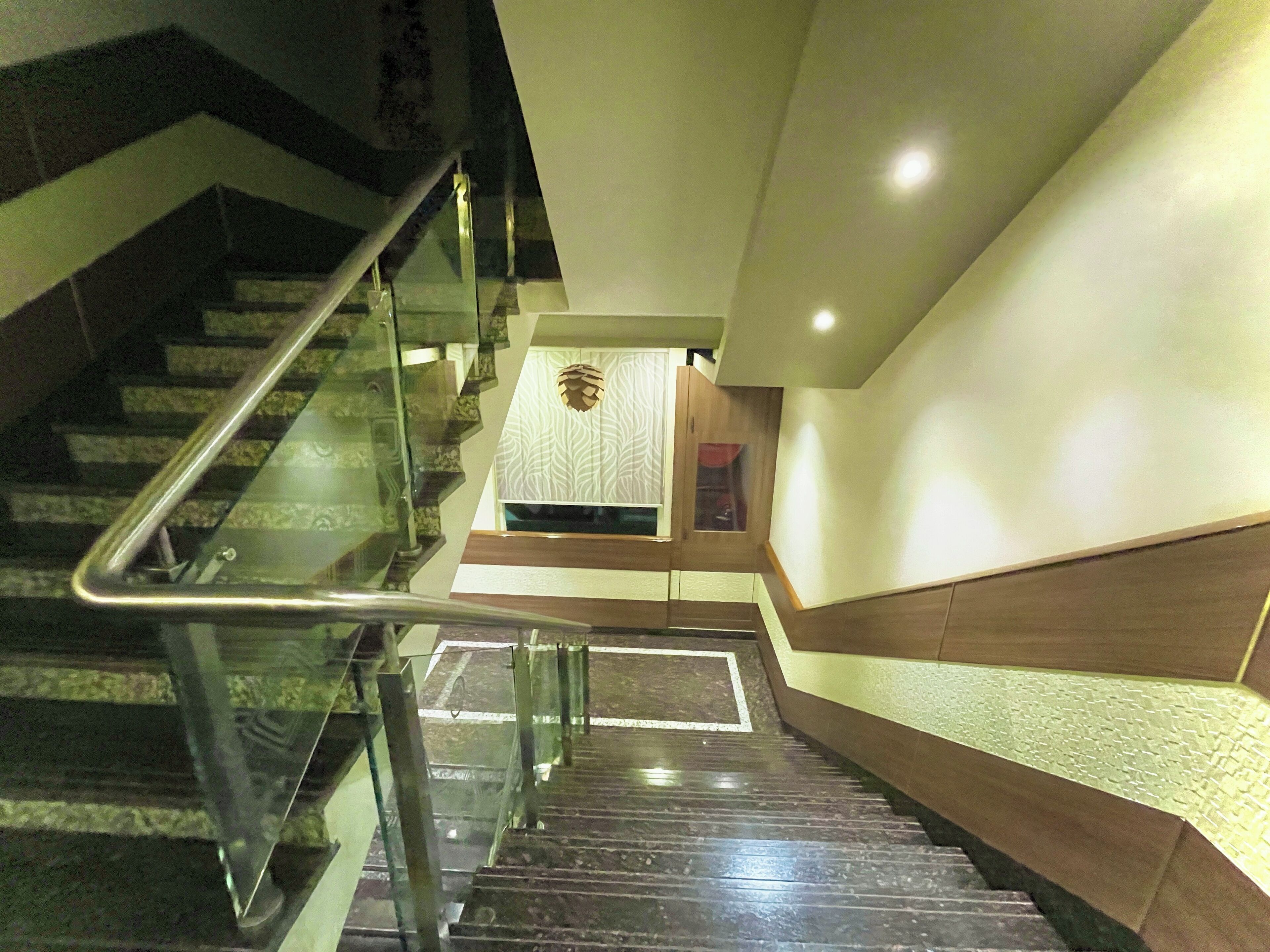 Una escalera con barandillas de vidrio y peldaños de madera que lleva a un rellano con un muro estampado y una pequeña mesa.