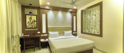 Habitación de hotel con cama, escritorio, silla, ventilador de techo y ventana con vista decorativa.