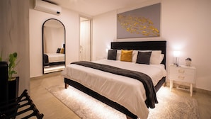 Une chambre à coucher moderne avec un grand lit, des tables de chevet, un miroir et une œuvre d’art murale.