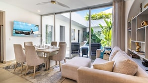Un salon moderne comprenant un coin repas, de grandes portes-fenêtres coulissantes donnant sur un balcon et un téléviseur fixé au mur.