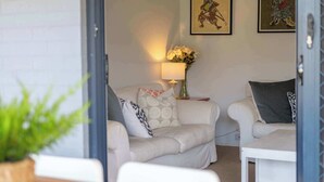 A cozy living room with two white sofas, a small table, and a vase of flowers. - Blue House on Pippi - Oceanstays - Pet Friendly (Yamba)