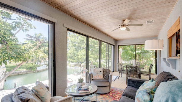 A spacious living room with large windows, a ceiling fan, and a view of a water body and greenery outside. - Endless Summer Retreat: Dog-Friendly 3BR Canal Front Oasis, Dockage & Easy Atlantic/Gulf Access (Cudjoe Key)