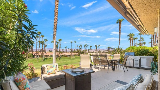 An outdoor patio with wicker furniture, a grill, and a view of a golf course. - Palm Valley CC Charm | Outdoor Dining on the Patio, Desert Fun, Fitness, Spa, Tennis & Pickle Ball (Palm Desert)