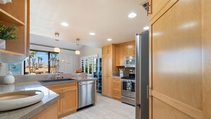 A modern kitchen with wooden cabinets, stainless steel appliances, and a large island with a sink. - Palm Valley CC Charm | Outdoor Dining on the Patio, Desert Fun, Fitness, Spa, Tennis & Pickle Ball (Palm Desert)