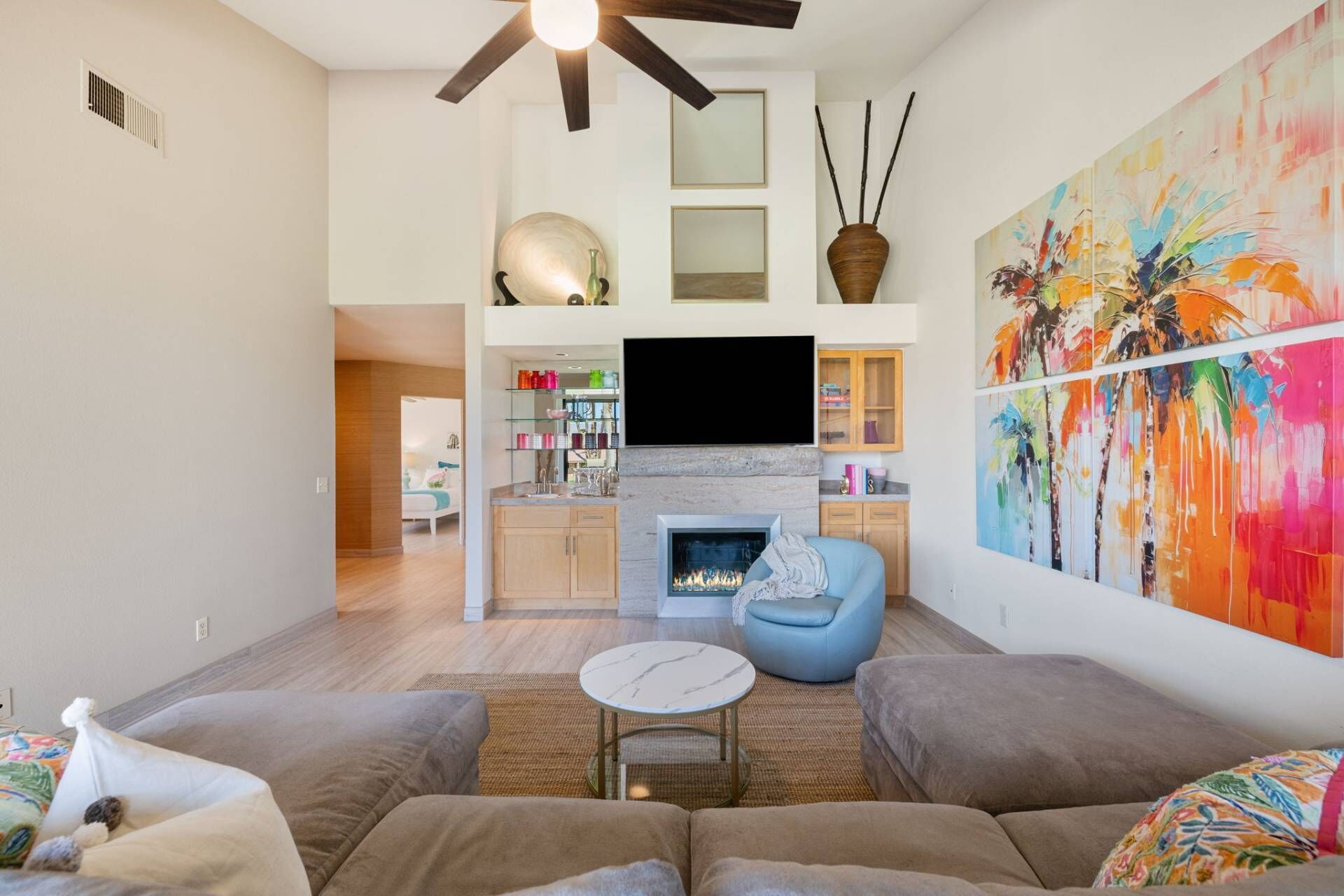 Una sala de estar moderna con chimenea, un televisor grande y un cuadro abstracto de colores.