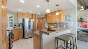 A modern kitchen with wooden cabinets, stainless steel appliances, and a central island with stools. - Palm Valley CC Charm | Outdoor Dining on the Patio, Desert Fun, Fitness, Spa, Tennis & Pickle Ball (Palm Desert)