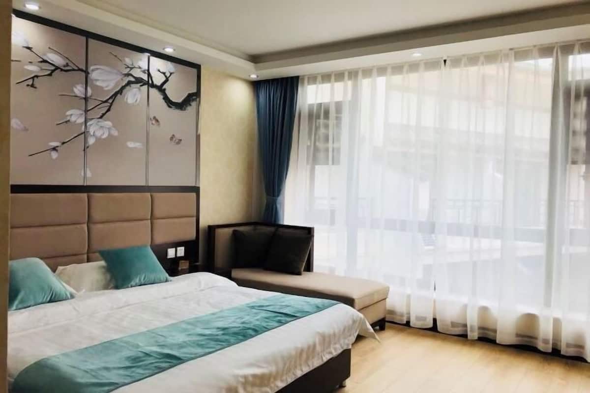 Une chambre d’hôtel avec un lit, un canapé, une œuvre d’art accrochée au mur et une grande fenêtre ornée de rideaux légers.