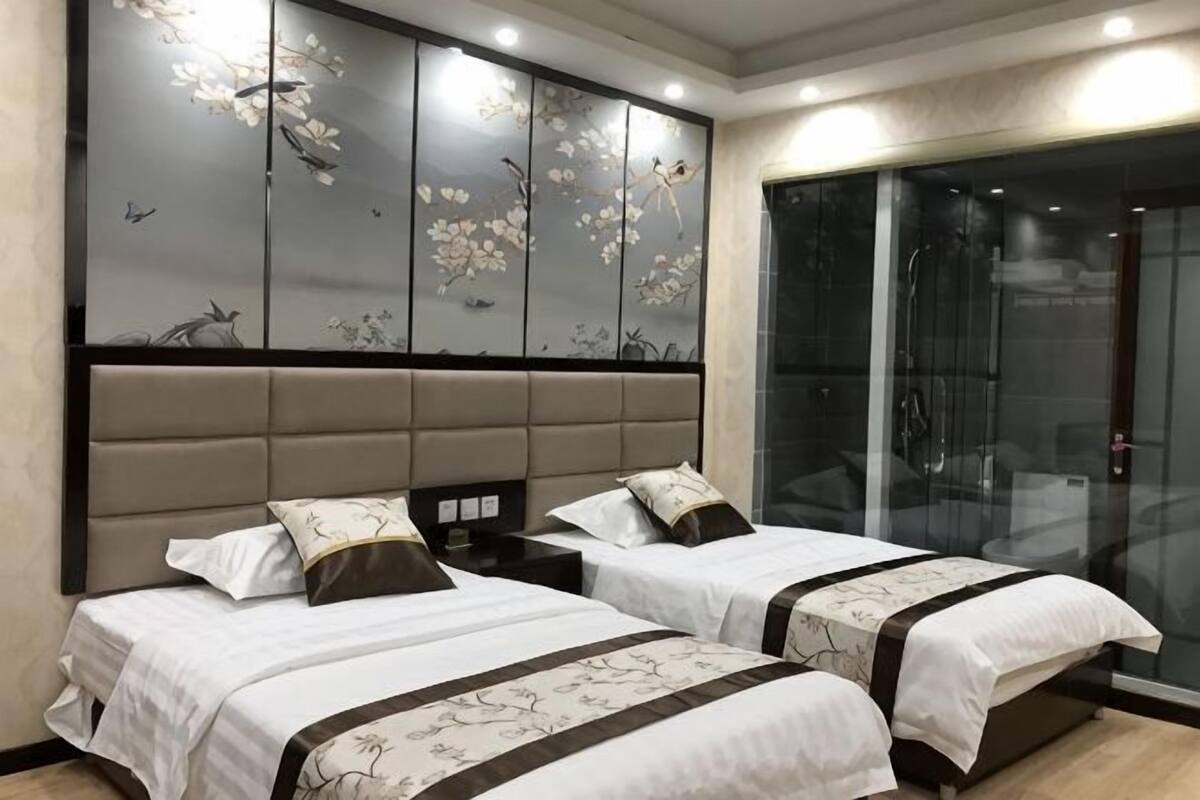 Une chambre d’hôtel avec deux lits, un grand mur décoratif et une porte coulissante en verre donnant sur l’espace de la douche.