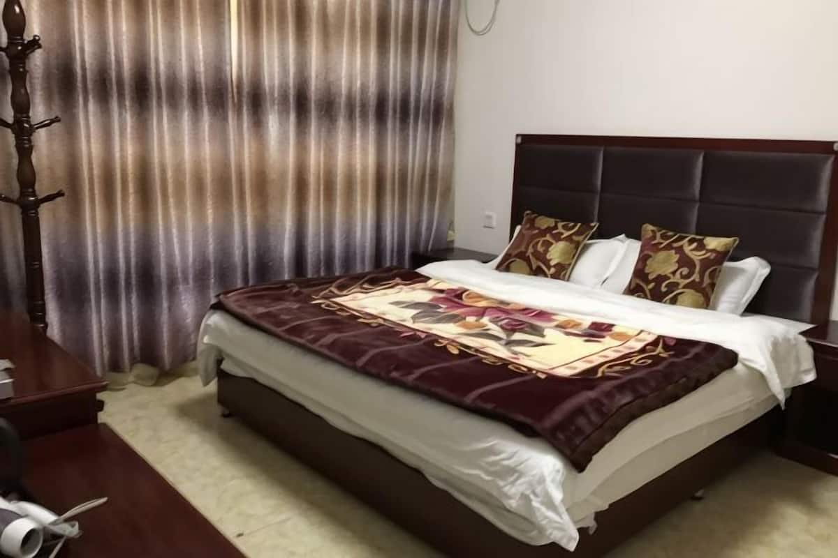 Une chambre d’hôtel avec un grand lit, une tête de lit, un rideau et une table de chevet en bois.