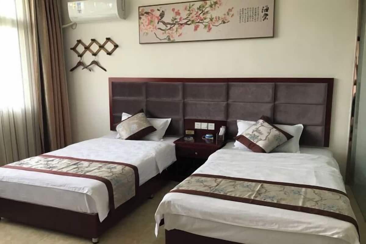 Une chambre d’hôtel avec deux lits, une tête de lit en bois, un climatiseur fixé au mur et une œuvre d’art encadrée.