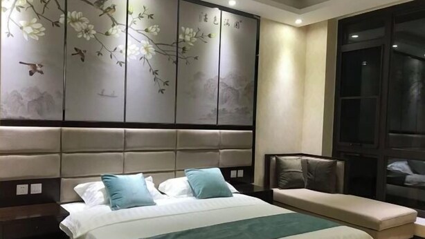 Une chambre d’hôtel avec un grand lit, un banc, un mur décoré d’œuvres d’art et une fenêtre.