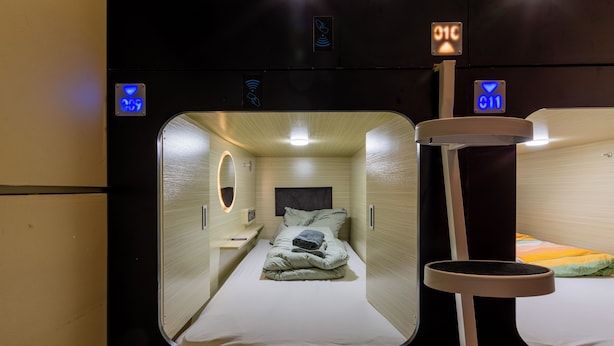 A compact, well-lit train compartment with two beds, each with a pillow and blanket, and a small table. - MUE Cubes (Basel)
