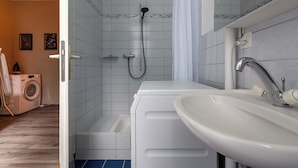 A bathroom with a shower, a sink, and a washing machine. - MUE Cubes (Basel)