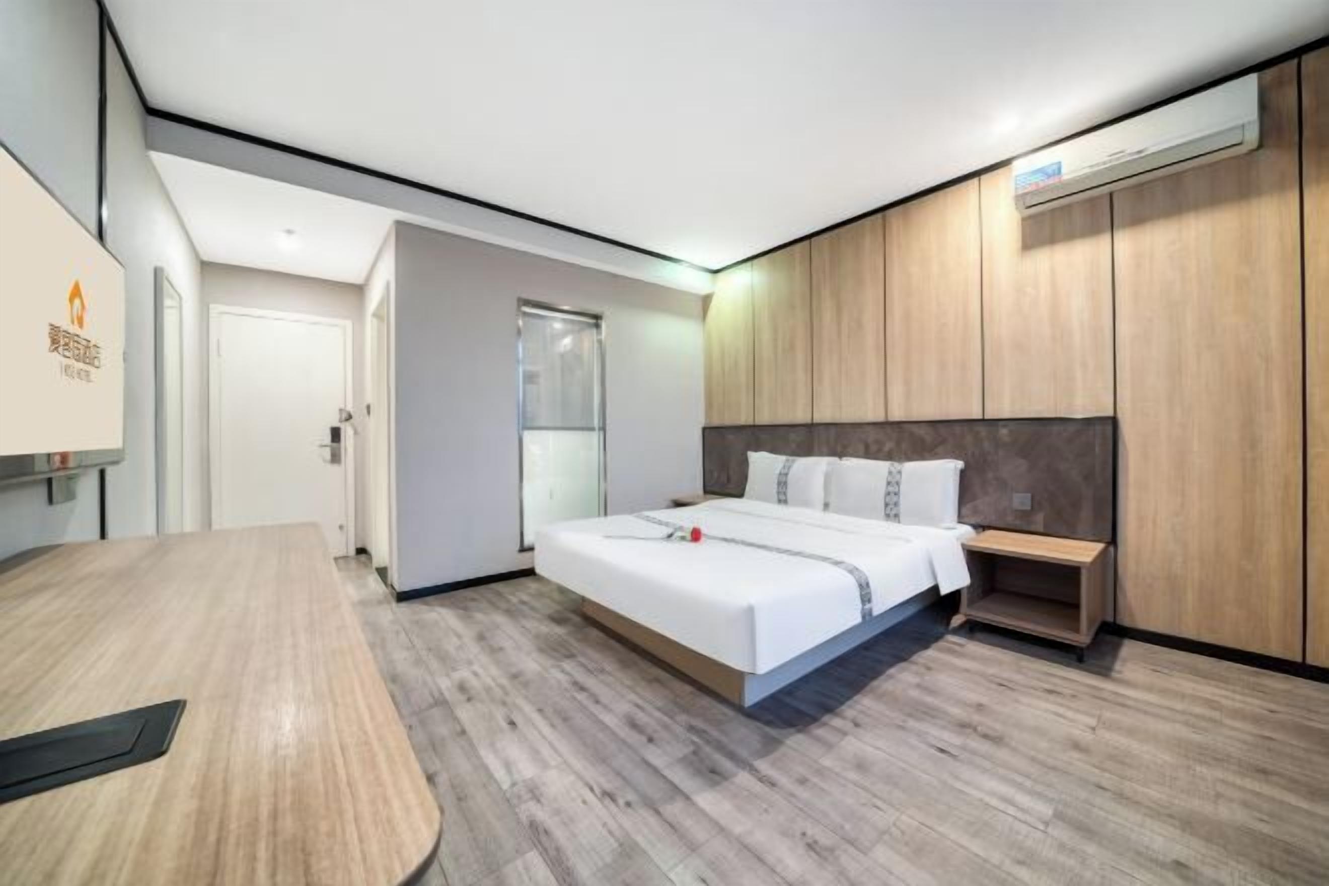 Une chambre d’hôtel moderne avec un grand lit, une armoire en bois, un bureau et une porte en verre donnant accès à la salle de bain.
