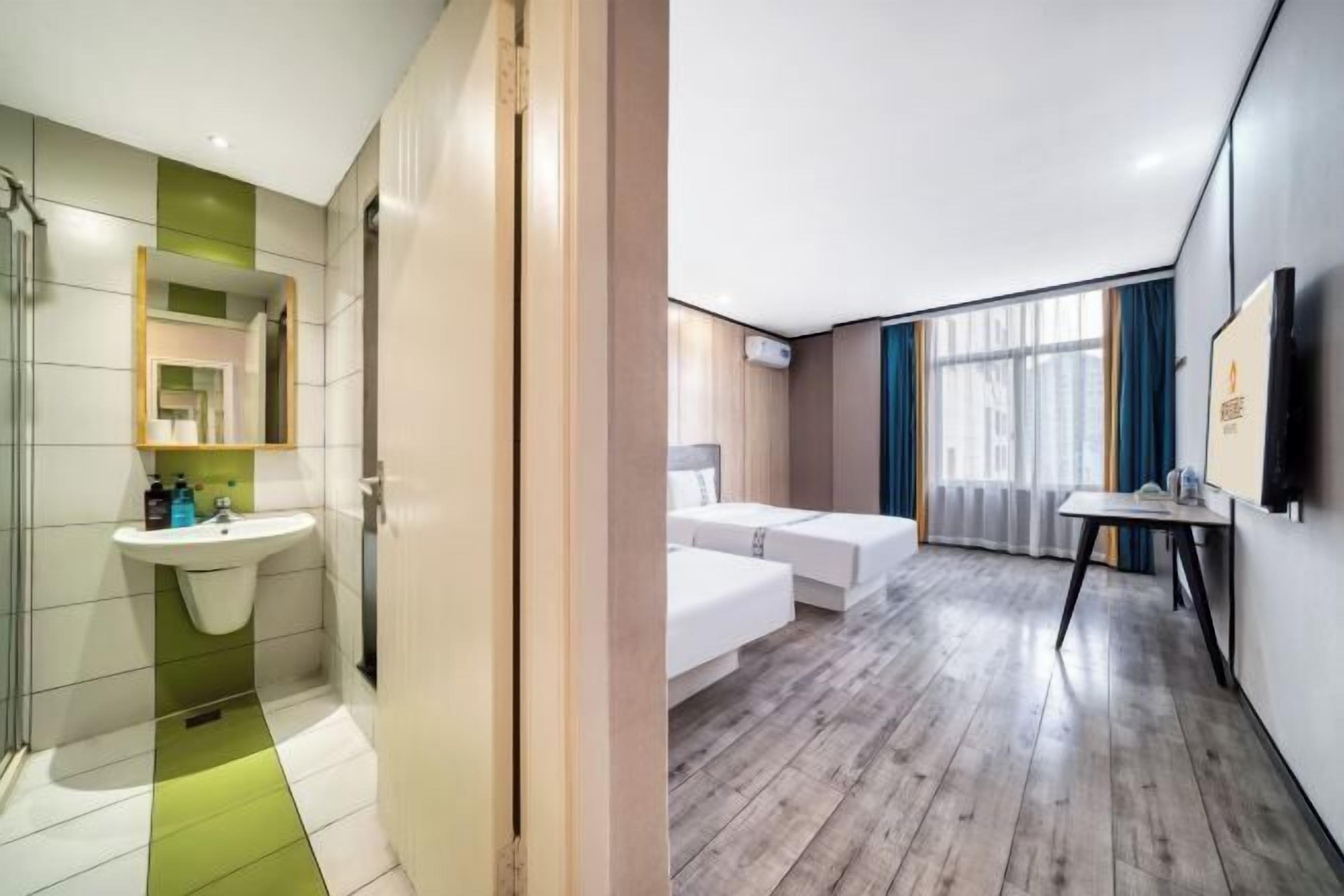 A modern hotel room with a bathroom, a bed, a desk, and a large window.