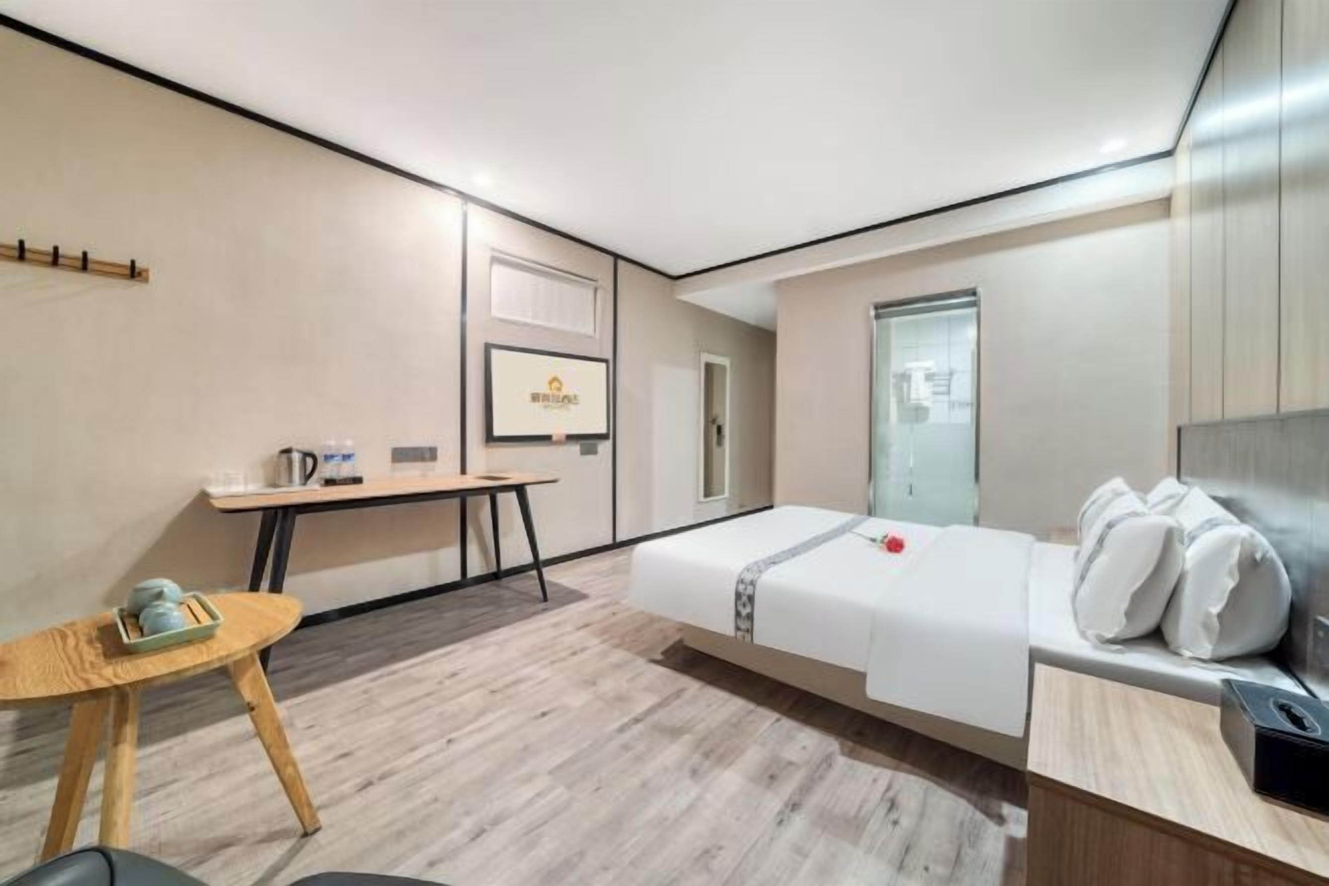 A modern hotel room with a bed, bedside table, and a small desk with a chair.