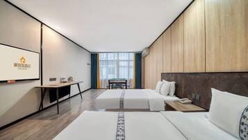 A hotel room with two beds, a desk, and a view of the city.