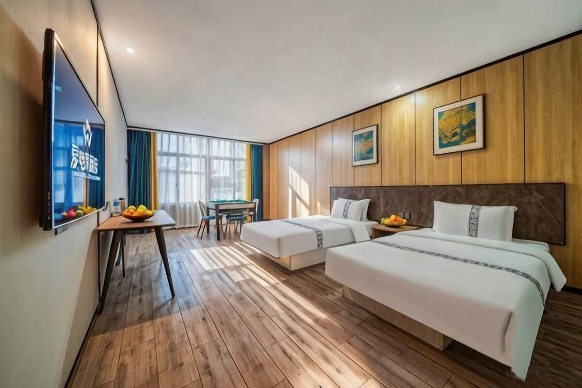 Habitación de hotel con dos camas, un escritorio, una silla, un televisor y un ventanal grande.