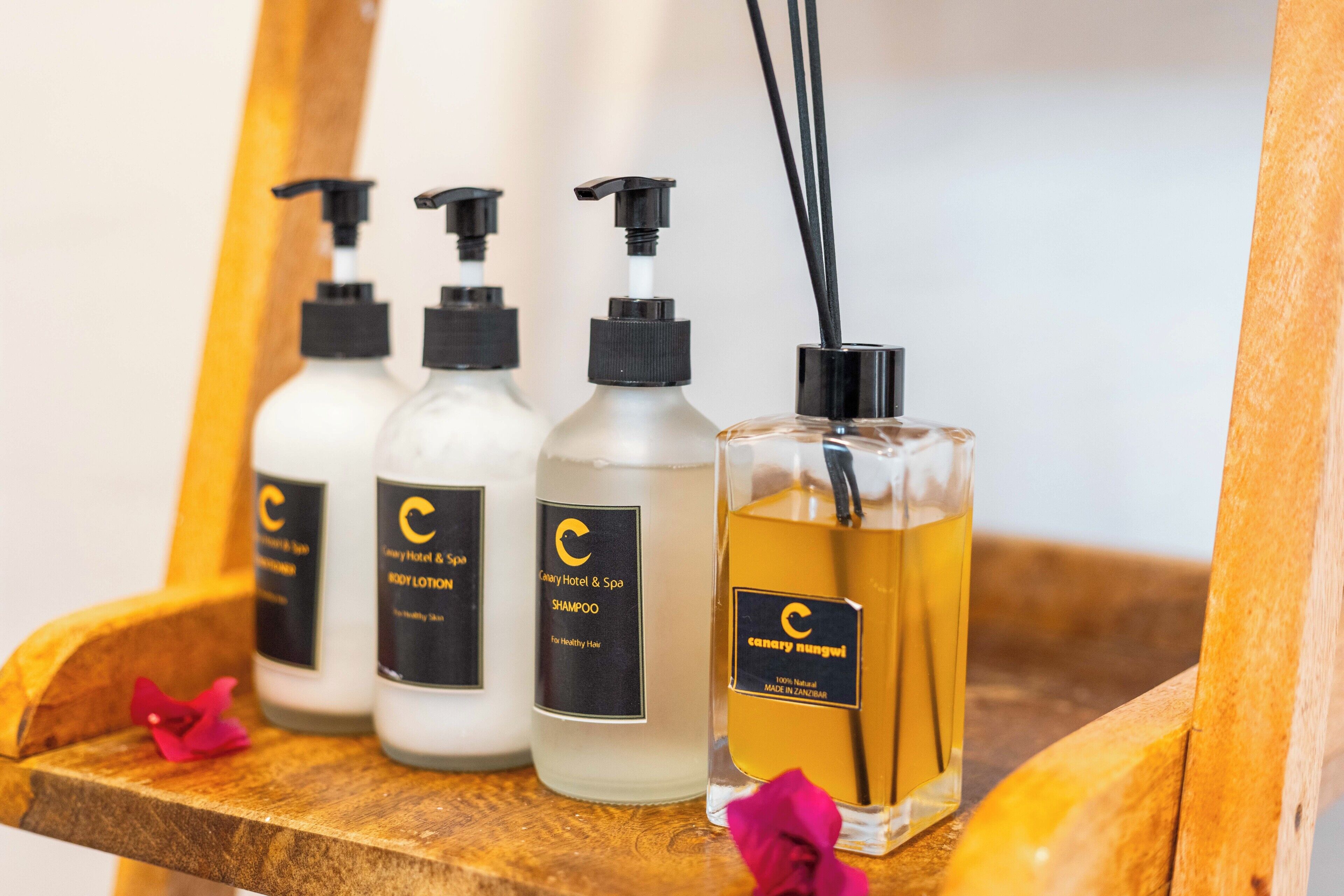 A wooden shelf with four bottles of hotel products and a glass bottle of perfume.