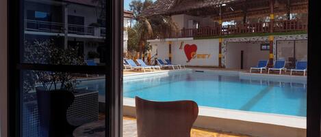 Vista a la piscina con sillones de jardín, una silla y un edificio con un cartel que dice 'I love Canary'.