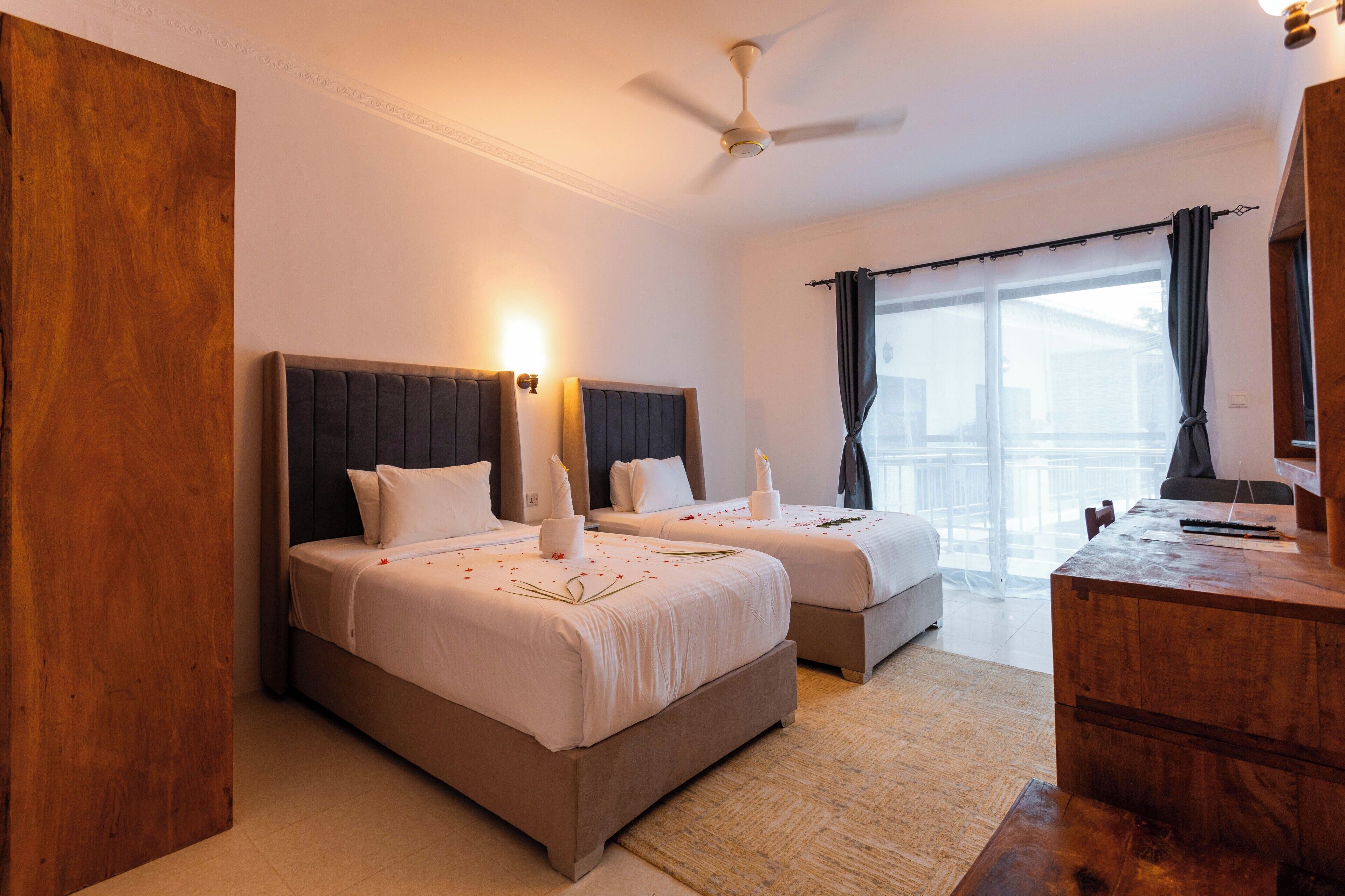 Una habitación de hotel con dos camas, un aparador de madera y un ventanal con cortinas.