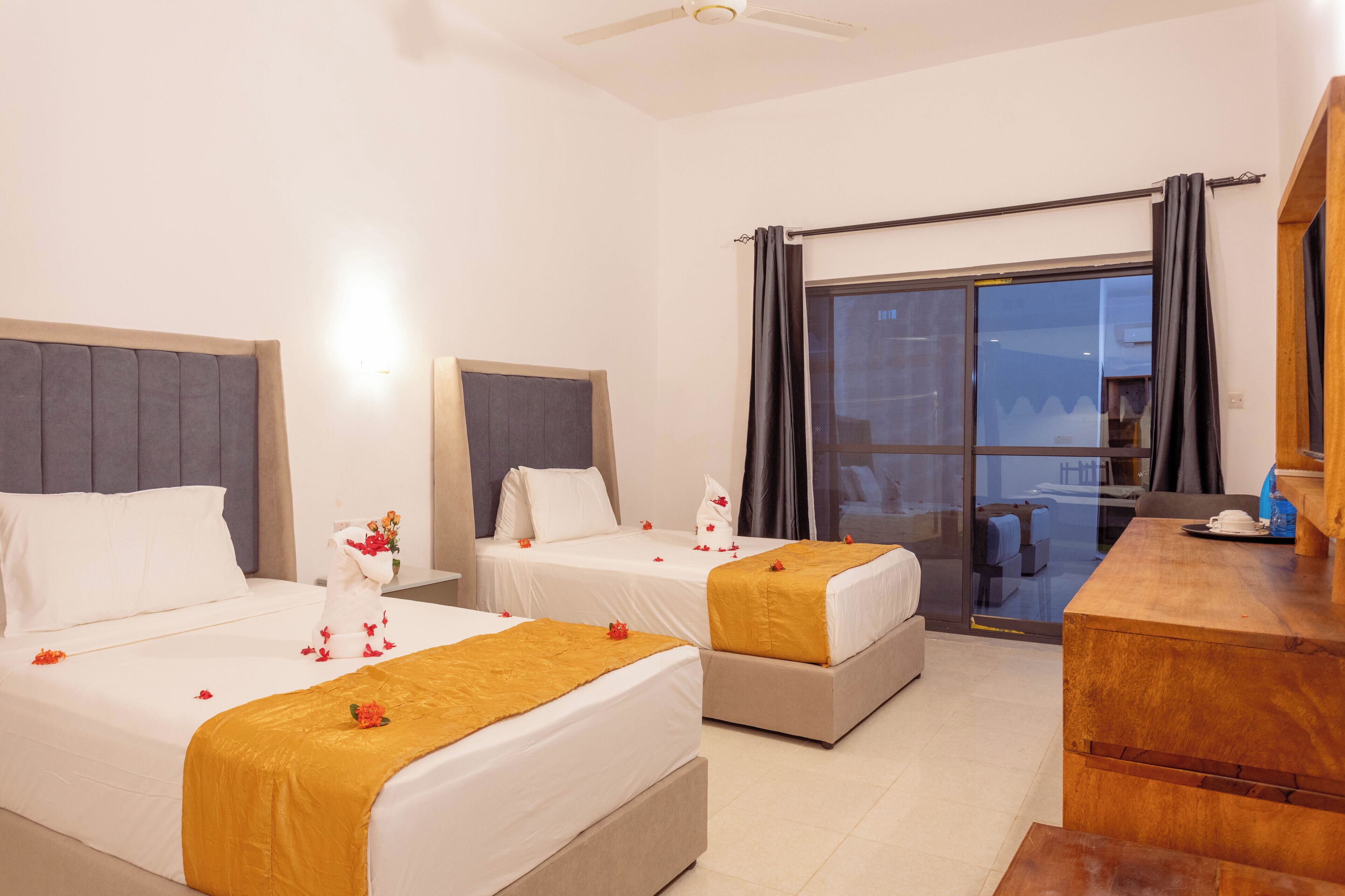 A hotel room with two beds, a wooden desk, and a sliding glass door leading to a balcony.